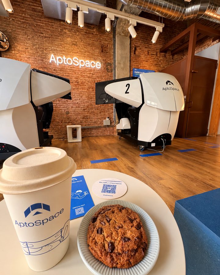 Café y galleta de AptoSpace en primer plano, con los simuladores de conducción al fondo