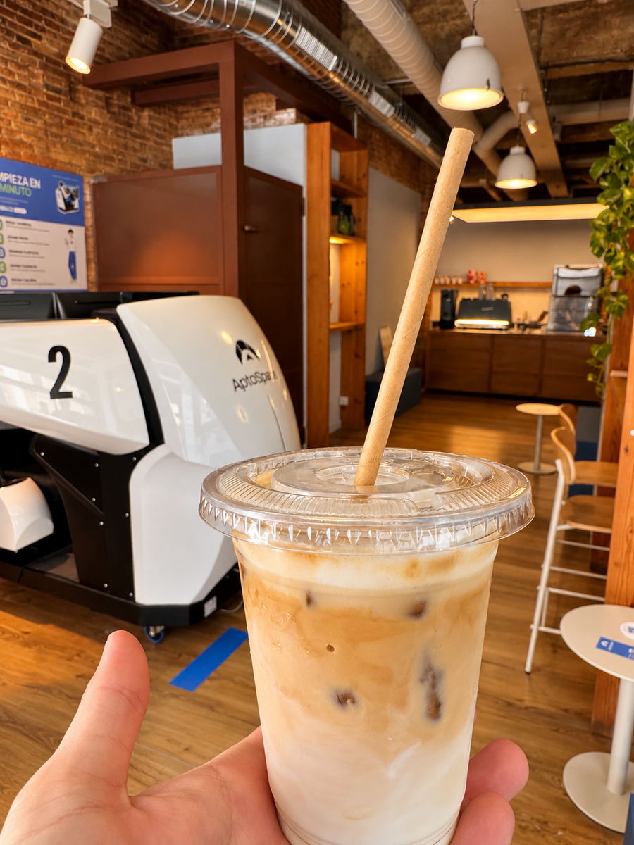 Café helado para llevar en la sala de AptoSpace, con el simulador 2 al fondo